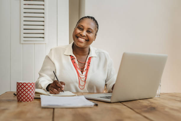 uśmiechnięta afroamerykanka przedsiębiorca pracujący z domu - working at home mature adult small business laptop zdjęcia i obrazy z banku zdjęć