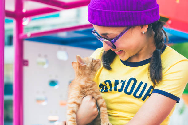 Happy girl with hat and sunglasses holding sweet ginger kitten.