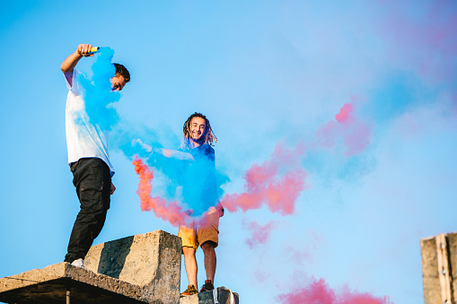 Two young Caucasian men releasing a colored smoke bomb on rooftop.