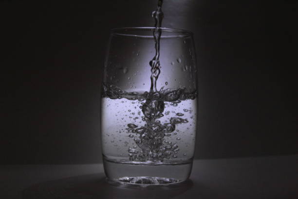 istock Water falling into the transparent / white glass with black background with some light 1180018212