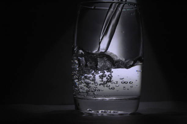 istock Water falling into the transparent / white glass with black background with some light 1180018262