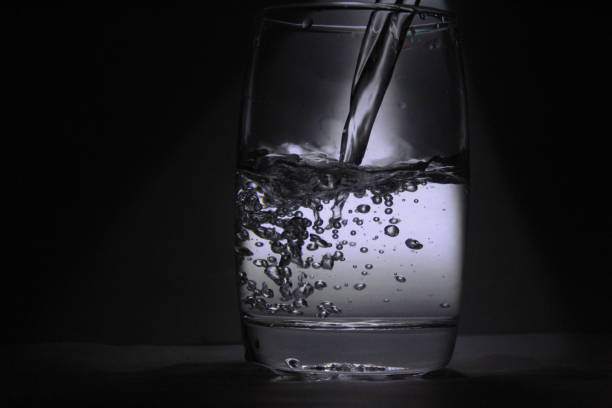 istock Water falling into the transparent / white glass with black background with some light 1180018280