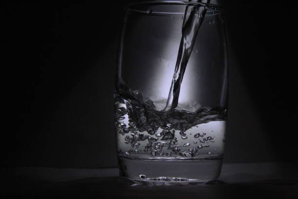 istock Water falling into the transparent / white glass with black background with some light 1180018290