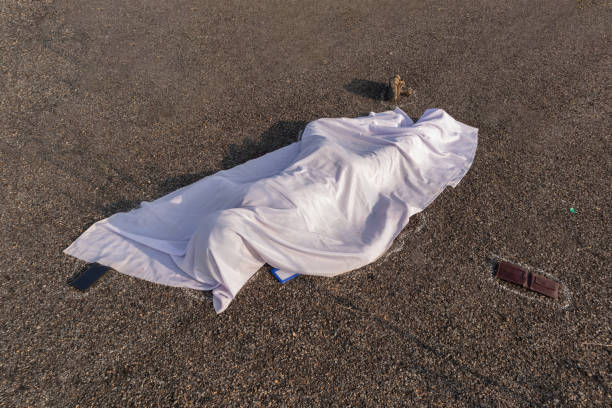 Concept of road accident scene, High angle view of chalk outlined dead body covered under white cloth laying on road. Concept of road accident scene, High angle view of chalk outlined dead body covered under white cloth laying on road colliding photos stock pictures, royalty-free photos & images