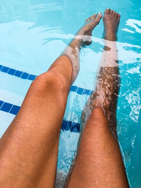 istock Young woman’s long tan legs in pool blue water 1180021159