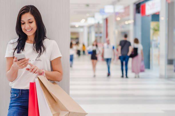 istock Black Friday, Woman using smartphone and holding shopping bag while standing on the mall background. 1180021318