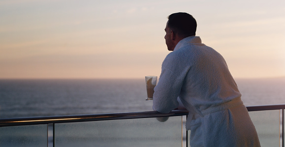Cropped shot of a handsome young man looking thoughtful while having coffee on the balcony of a beach house