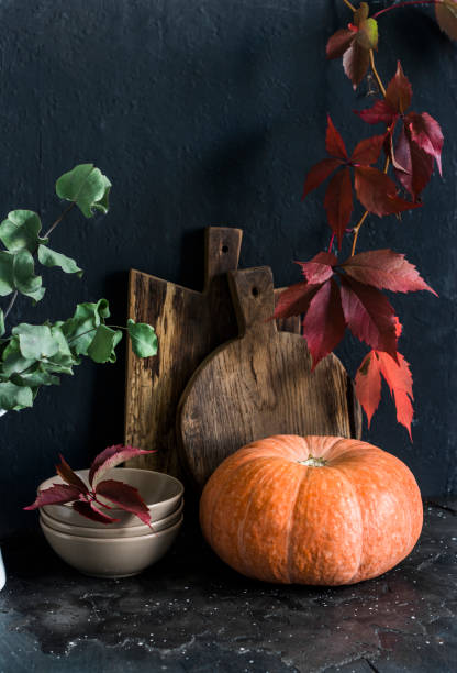 istock Fall kitchen still life. Crockery, eucalyptus branches, cutting boards, autumn leaves, pumpkin on the table, on a dark background. Rustic style. Flat lay 1180032030