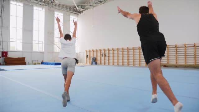 Two sportsman doing a cartwheel and a double back flip, steadicam, slow motion.