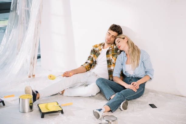 istock exhausted couple sleeping while sitting by white wall near roller tray with yellow paint 1180038426