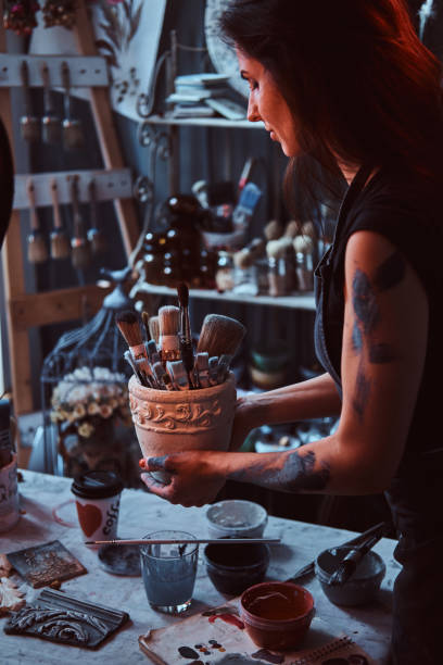 istock Young attractive painter is holdind jar with brushes in her own cozy workshop 1180043314