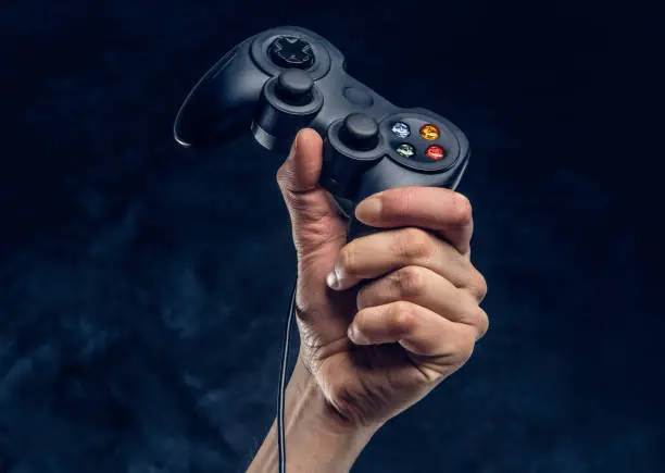 Photo of Video game console controller in gamer hand against the background of the dark wall