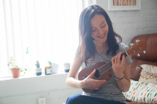 istock Young Asian woman practicing ukulele at home waist up version 1180049252