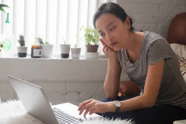 Young Asian woman looking online for work with serious expression in her living room.