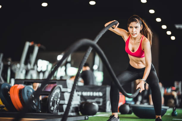 Beautiful Asian woman exercise on battling ropes training equipment in indoor fitness gym. Sport recreational activity, people workout, or healthy lifestyle concept stock photo