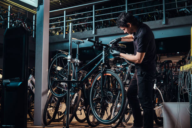 Expirienced young master is repairing customer's bicycle at workplace stock photo