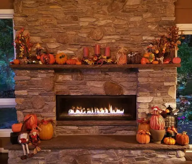 Brown toned custom stone fireplace with a display in orange colors of pumpkins of various sizes and other autumn decor set up on this large masonry hearth and mantle.