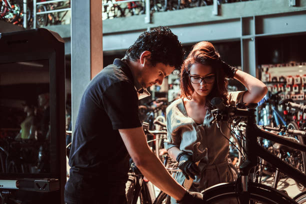 istock Young master and his attractive apprentice are fixing customer's bicycle at workshop 1180063588