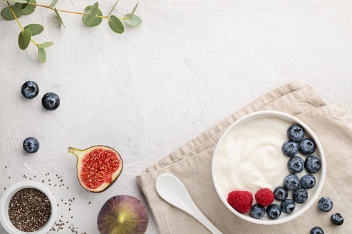 natural healthy superfood fermented yogurt with blueberry, figs, chia seeds and raspberry in white  bowl on light gray table. Image is copy space and top view