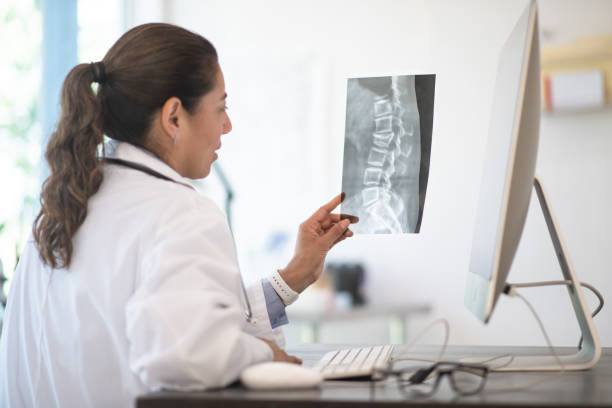 A Doctor Reviewing X-ray Results stock photo A Doctor reviewing her patients x-ray results for possibly breaks, fractures and abnormalities spine stock pictures, royalty-free photos & images