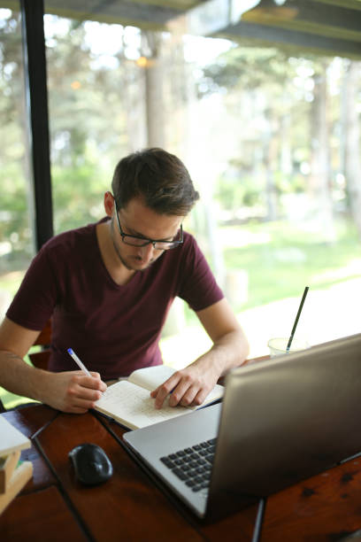 istock Young businessman taking note beside laptop on table in cafe 1180077772