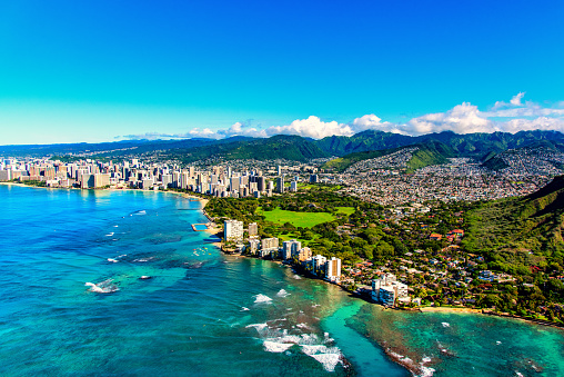 The entire coastline of Honolulu, Hawaii including the base of Diamond Head crater and state park, past the hotel lined Waikiki Beach towards downtown in the distance including the suburban neighborhoods dotting the hills surrounding the city center.