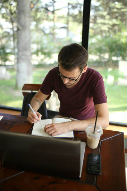 istock Young businessman taking note beside laptop on table in cafe 1180086113