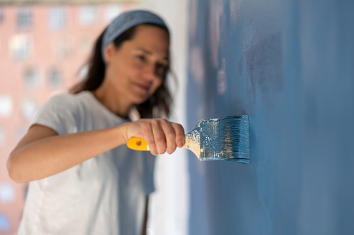 Close-up on a woman painting her house with focus on the brush â home improvement concepts