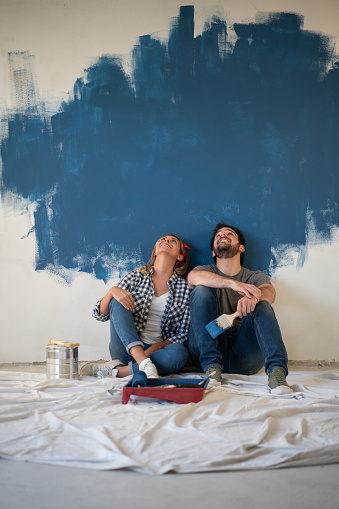 Thoughtful couple taking a break from painting their house blue - home improvement concepts