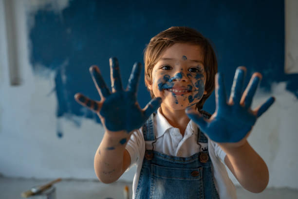 Portrait of a happy Latin American boy having fun painting the house blue and showing his hands full of paint - home improvement concepts
