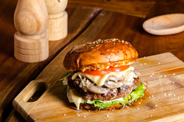 istock new large hamburger burger with meat, bacon, sausage, lettuce, champignons, pineapple and tomatoes, sauce and cheese standing on a wooden cutting kitchen board, on the table 1180089608