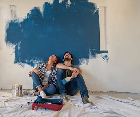 Thoughtful couple painting their house and looking up to the wall â redecorating concepts