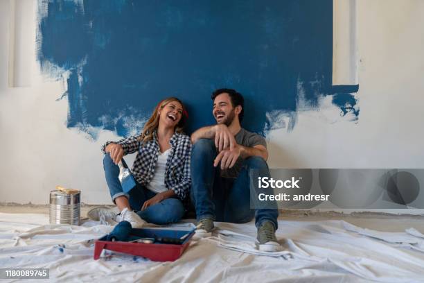 Happy Couple Laughing While Taking A Break From Painting Stock Photo - Download Image Now