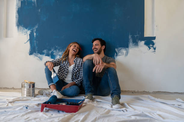 happy couple laughing while taking a break from painting - pintar parede imagens e fotografias de stock