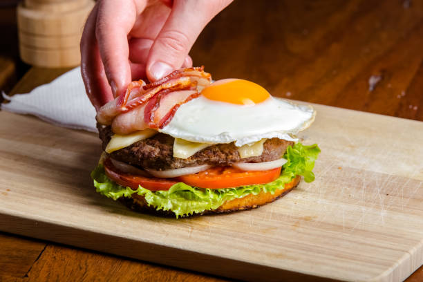 istock new large hamburger burger with meat, bacon, sausage, lettuce, champignons, pineapple and tomatoes, sauce and cheese standing on a wooden cutting kitchen board, on the table 1180089889