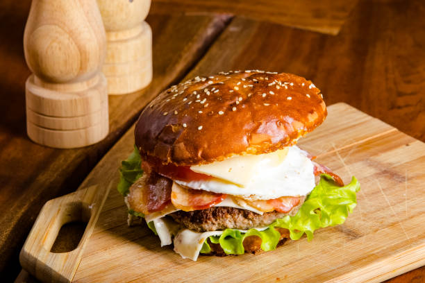 istock new large hamburger burger with meat, bacon, sausage, lettuce, champignons, pineapple and tomatoes, sauce and cheese standing on a wooden cutting kitchen board, on the table 1180089971