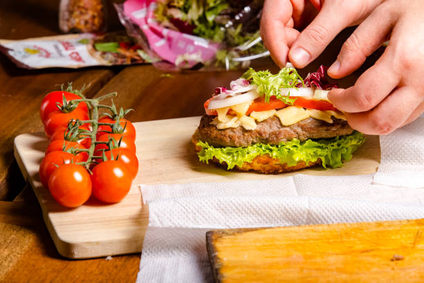 istock new large hamburger burger with meat, bacon, sausage, lettuce, champignons, pineapple and tomatoes, sauce and cheese standing on a wooden cutting kitchen board, on the table 1180091313