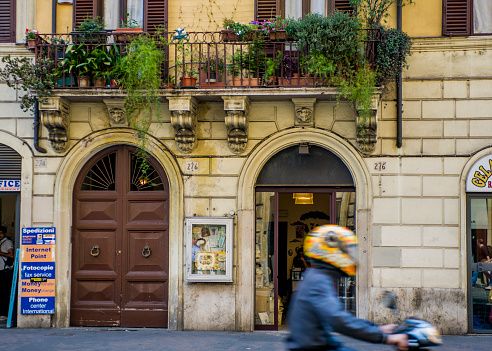 Image taken in a street in Rome Italy, showing the classic Italian architecture with a blurred Vespa rider and Italian transport.