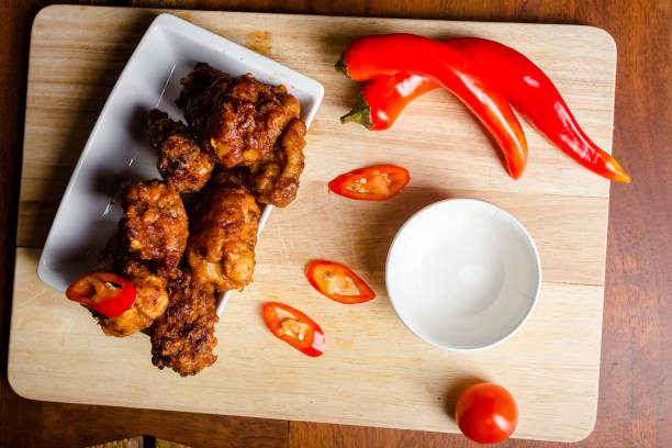 new Fried chicken nuggets legs of a wing with a crispy crust, lie in a handful on salad greens, on a wooden kitchen cutting board, spices are scattered, knives, pepper shaker, salt, stands on a wooden cutting kitchen board, on a parchment table nuevas pepitas de pollo frito patas de un ala con una corteza crujiente, se acuestan en un puñado en verduras de ensalada, en una tabla de cortar de la cocina de madera, las especias están dispersas, cuchillos, coctelera de pimienta, sal, se encuentra en