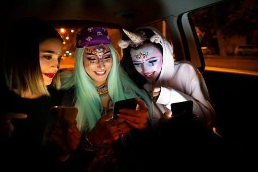 Girls riding in a taxi to Halloween party and using their cell phones.