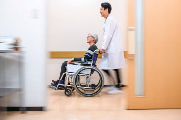 japanese doctor pushing patient in wheelchair down corridor - 3666 imagens e fotografias de stock