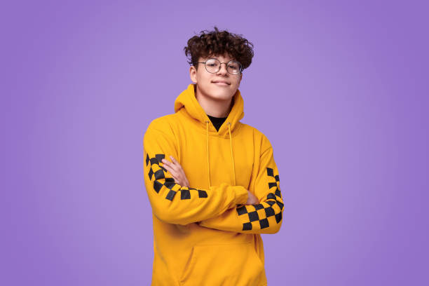 Confident youngster looking at camera Positive teen boy in yellow hoodie crossing arms and looking at camera against bright violet background multi coloured glasses stock pictures, royalty-free photos & images