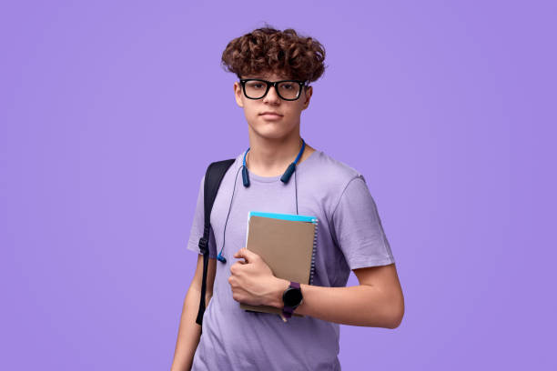 Teen student with notebooks looking at camera Confident youngster in glasses holding notepads and looking at camera during studies against vibrant violet background nerd teenager stock pictures, royalty-free photos & images
