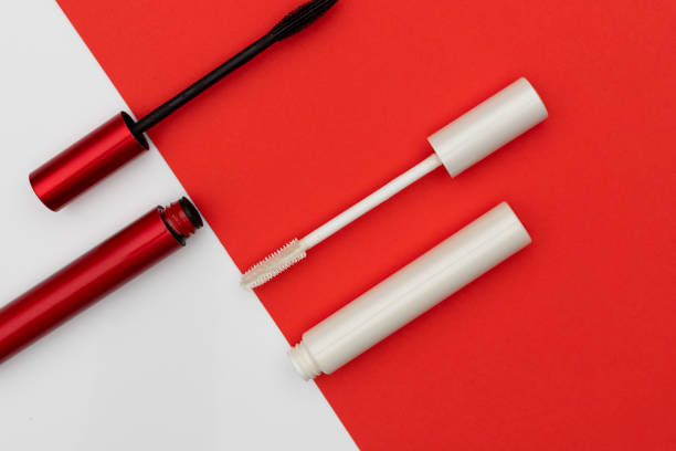From above tubes and brushes of black and white mascara placed near diagonal line of two colored background
