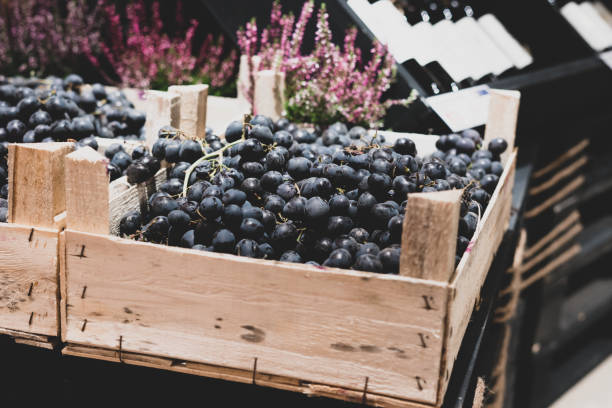 ciemne winogrona w drewnianym pudełku na kasie sklepowej. wino w tle. kreatywny handel, rozwiązania dekoracyjne. - wine bottle wine rustic liquor store zdjęcia i obrazy z banku zdjęć