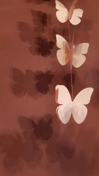 istock Patterned blurry shadows from butterfly 3D shaped paper elements of hanging garlands at marsala color background. Pink paper butterflies closeup. Abstract background. Zen-like decorations 1180132364