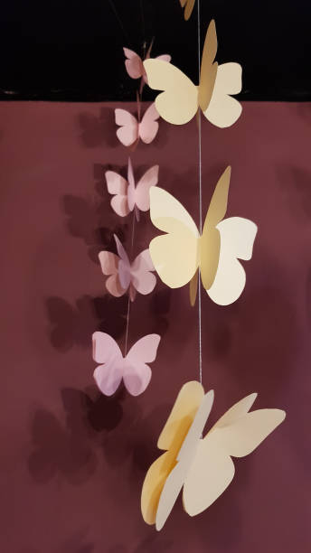 istock Three dimensional butterfly shaped paper elements of hanging garlands with blurry shadows on dark wall background. Beige color paper butterflies closeup. Abstract background. Zen-like decorations 1180132373