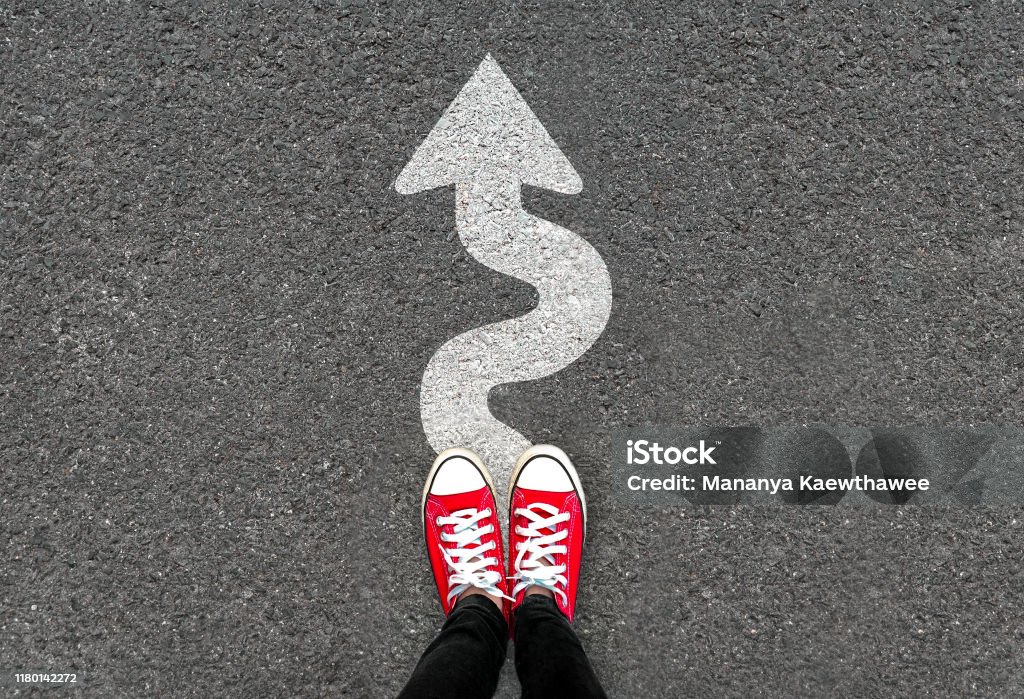 Feet and white arrow sign go straight on road background. Top view of woman. Forward movement and motivation idea concept. Feet and white arrow sign go straight on road background. Top view of woman. Forward movement and motivation idea concept. Selfie of foot and legs in red sneaker shoes on pavement floor from above. Footpath Stock Photo