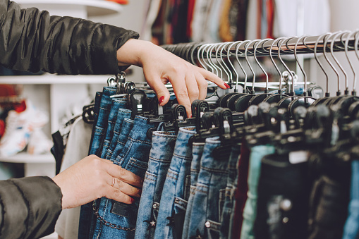 Concepto de moda rápida. Mujer elige jeans en una tienda. Mucha ropa en la tienda. Planeta Destructor de Moda Rápida photo