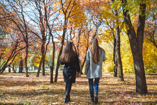 istock two girlfriends walking by autumn city park talking 1180150342